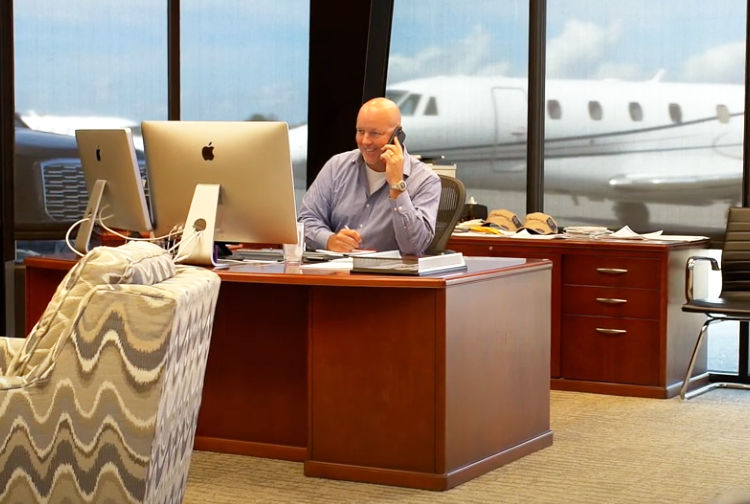 Jim Segrave working at his desk, a flyExclusive jet parked outside the window behind him