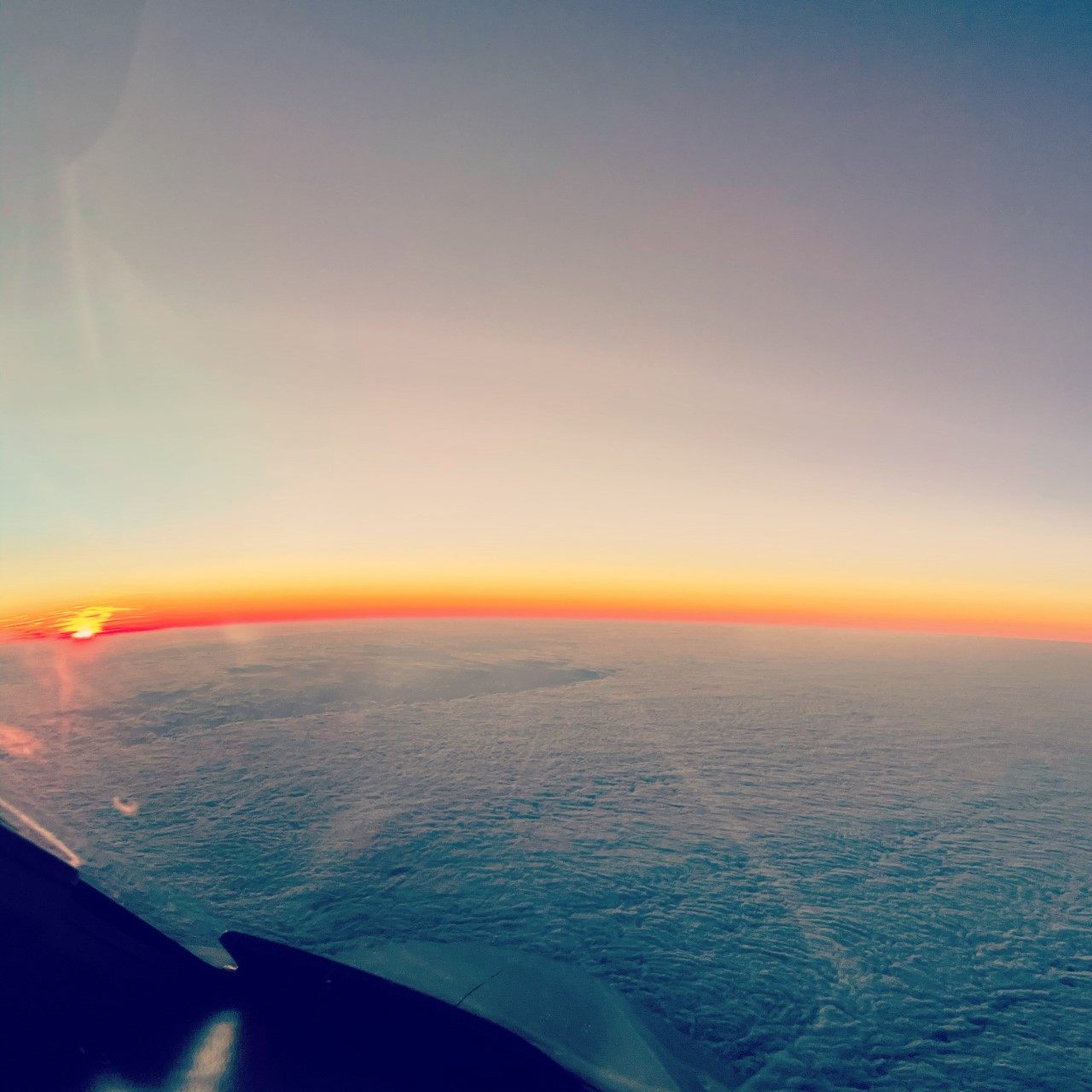 Sunset on the horizon above the cloud deck, seen past the wing