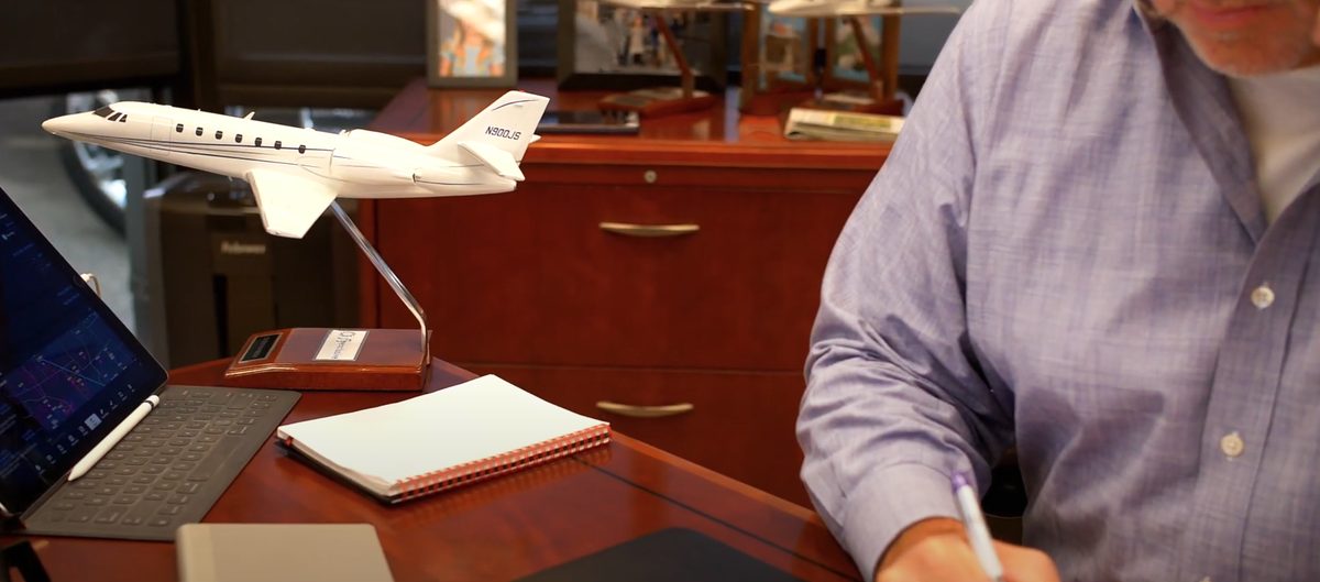 Jim Segrave writing at his desk beside a model of a flyExclusive Citation jet