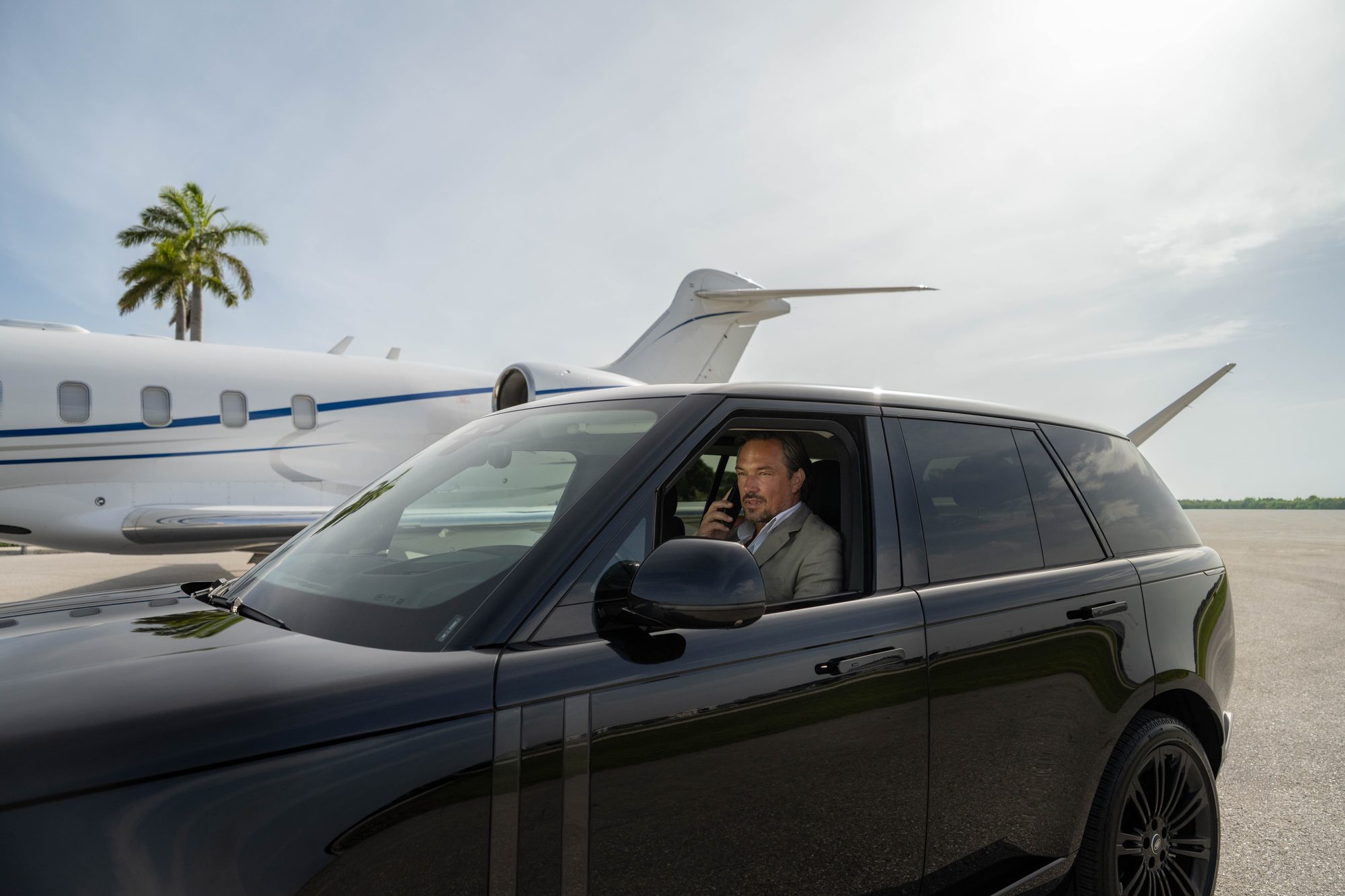 A member on the phone in a car on the ramp beside a waiting flyExclusive jet
